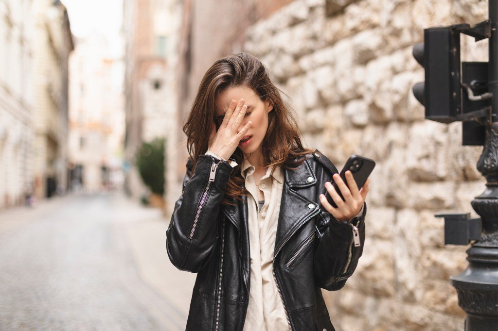 A sad woman holding a mobile phone and covering her face in distress