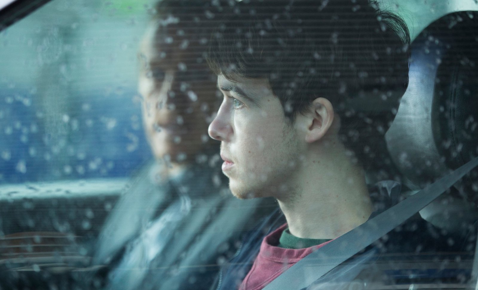 A young man drives a car, with an older man next to him.