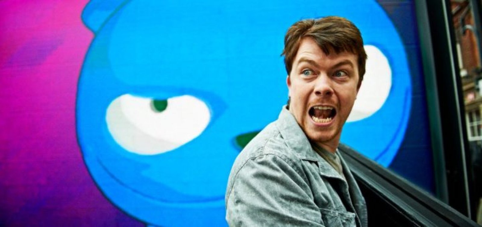 A man looks off camera, a looming animation behind him.