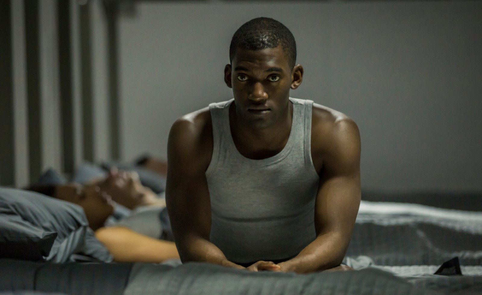 A Black man sits wearing a tank top.