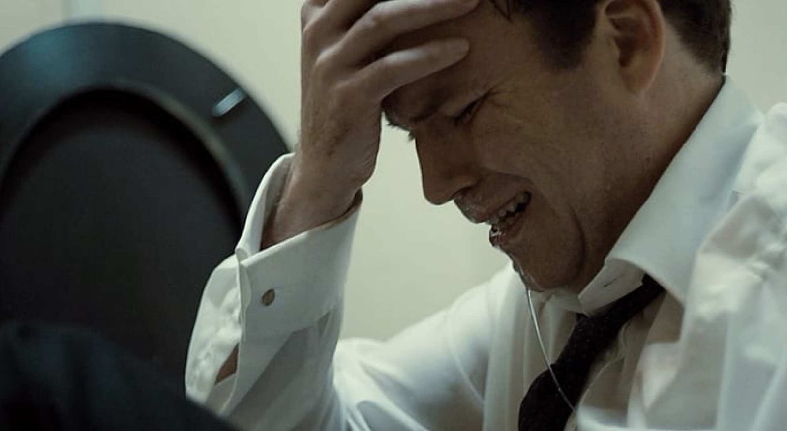A white man in business attire holds his head and grimaces.